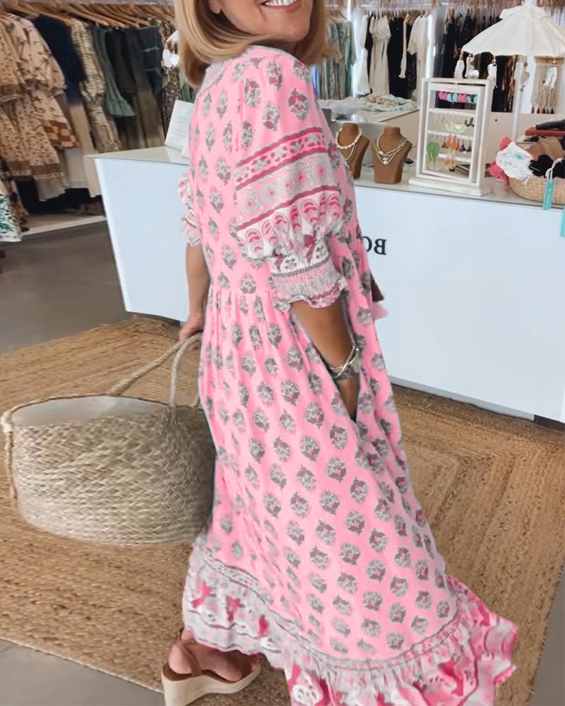 Pink - A woman wearing a light blue block-print maxi dress with a split V-neckline, tassel ties, and tiered skirt, holding a woven straw tote bag.