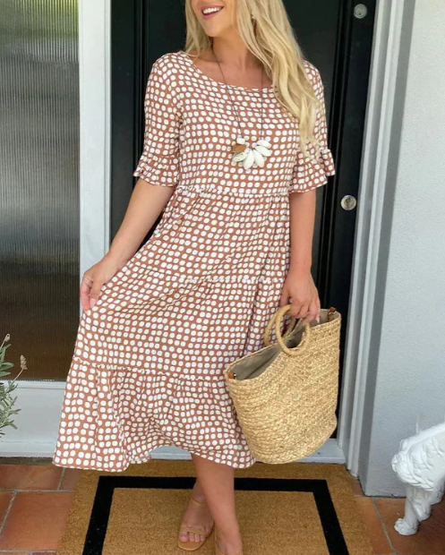 Black - A woman wearing a taupe and white dot print midi dress with a scoop neck, ruffled half sleeves, and a tiered skirt, holding a woven straw bag.