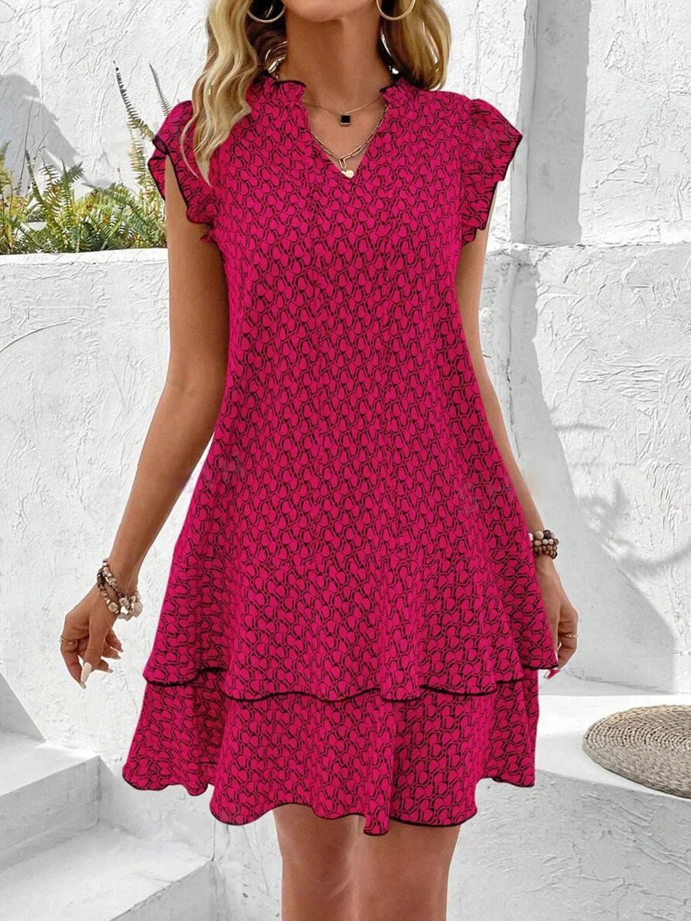 Red - A woman wearing a cream and black geometric print mini dress with flutter cap sleeves, a split neckline, and a tiered ruffle hem with dark contrast piping.