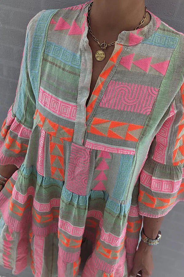 Colorful - A woman wearing a colorful geometric print tiered mini dress with a split neckline and three-quarter sleeves, featuring pink, orange, and green patterns on a textured fabric.