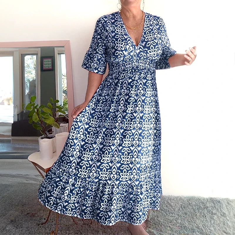 Navy - A woman wearing a teal green and white geometric ikat print midi dress with a smocked waist, V-neckline, flutter sleeves, and a tiered hem.