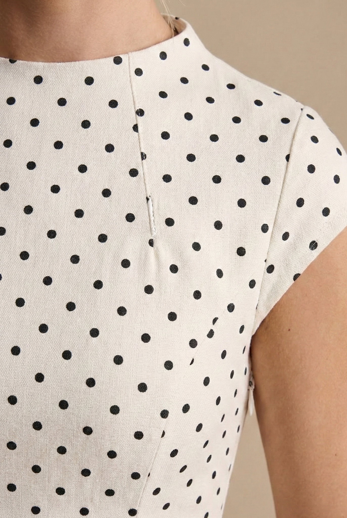 White - Model wearing a white and black polka dot maxi dress featuring a high neckline, cap sleeves, a fitted bodice with a basque waist, and a full pleated A-line skirt.
