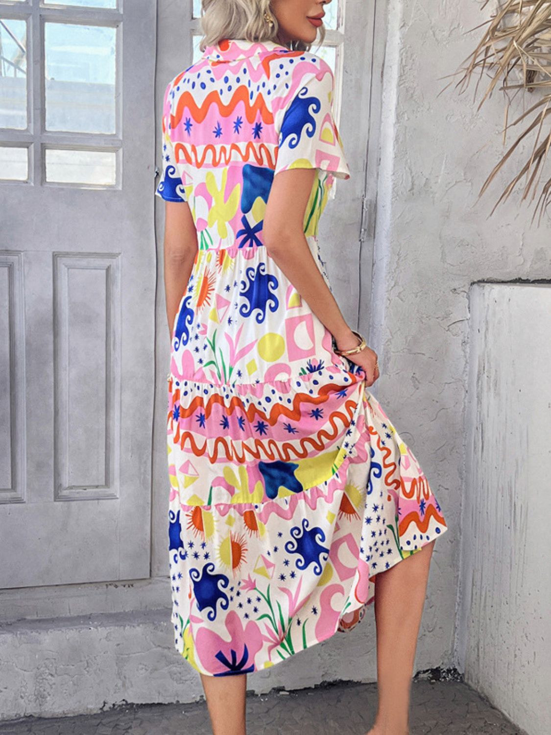 Multicolor - A woman wearing a short-sleeve, collared maxi dress with a colorful retro floral print, featuring a button-down front and a tiered skirt.