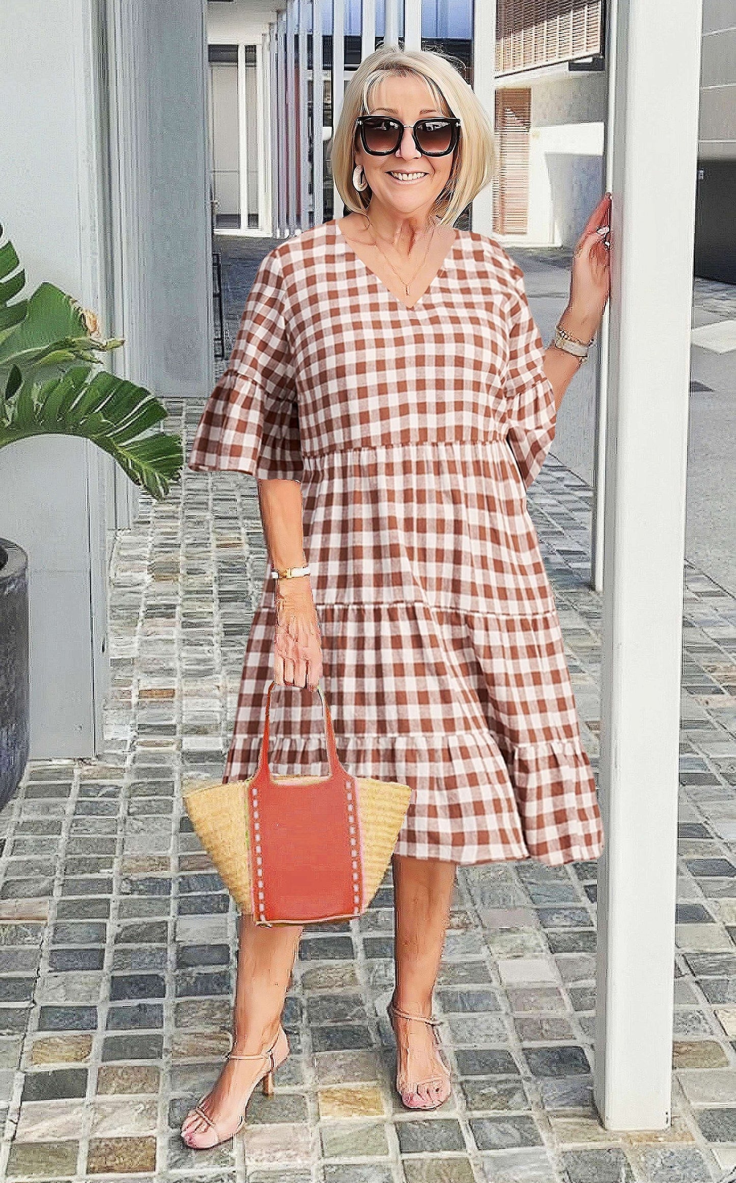 A woman wearing a blue and white speckled print midi dress with a V-neckline, elbow-length flutter sleeves, and a tiered skirt, holding a woven straw tote bag.