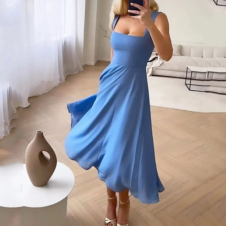 Blue - A woman wearing a white square-neck midi dress with a structured bodice and a flowing, double-layered chiffon A-line skirt, standing in a brightly lit minimalist room.