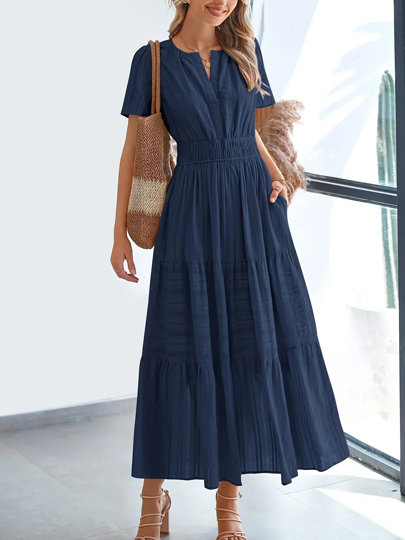 Navy Blue - A woman wearing a dusty pink, textured stripe maxi dress featuring a smocked waist, tiered skirt, short sleeves, and a split neckline, styled with a woven straw shoulder bag.