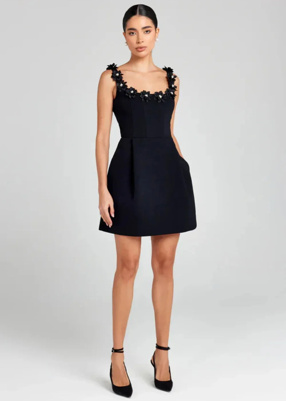 Black - Black structured crepe mini dress featuring a tailored bodice, A-line skirt with side pockets, and contrasting white 3D floral appliqués along the square neckline and shoulder straps.