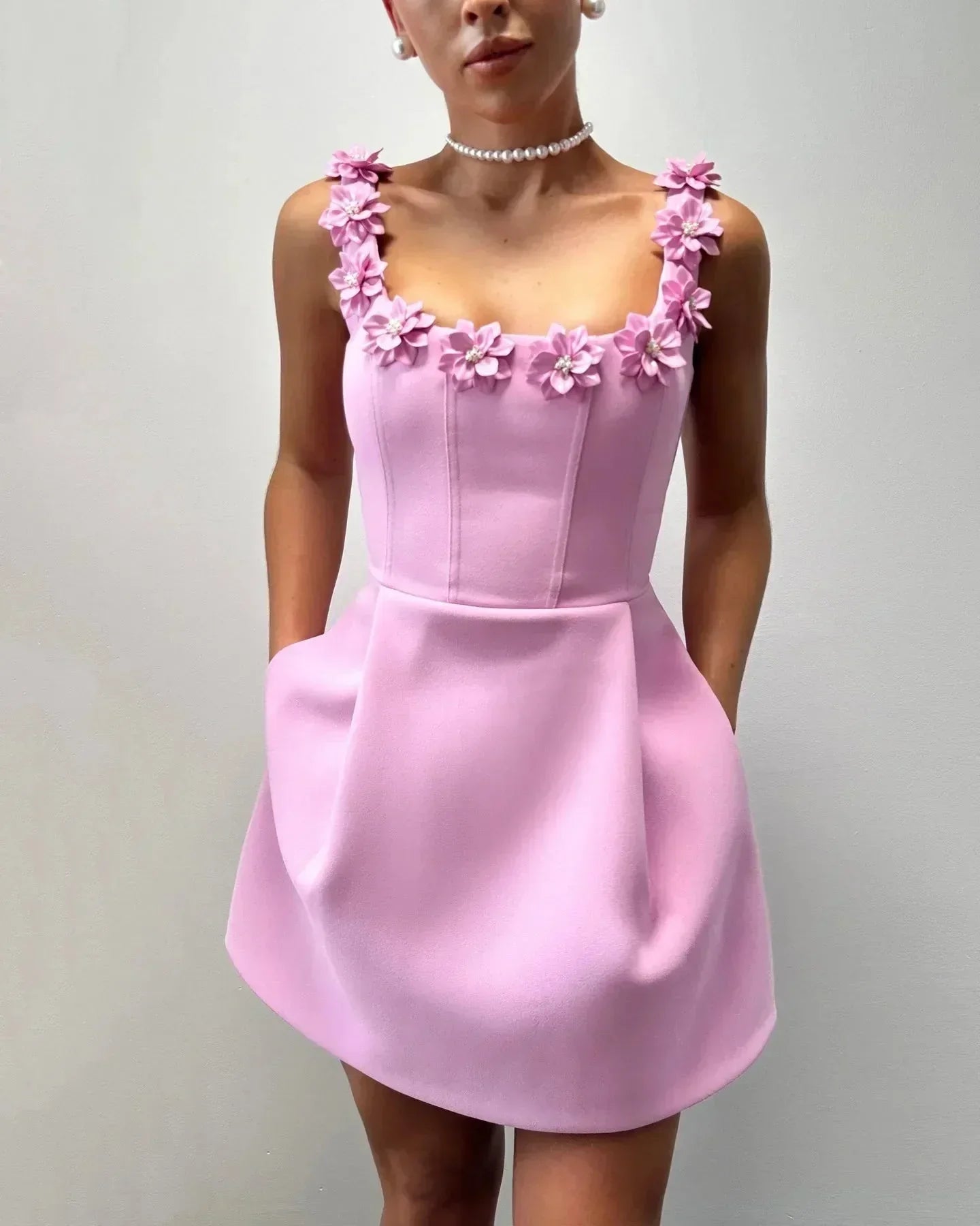 Pink - Sleeveless structured pink mini dress featuring a square neckline adorned with 3D floral appliqués, a tailored bodice with vertical seams, and a pleated A-line skirt with side pockets.