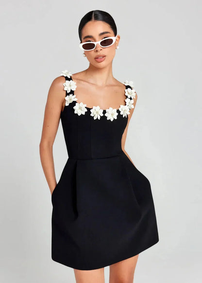 Black - Black structured crepe mini dress featuring a tailored bodice, A-line skirt with side pockets, and contrasting white 3D floral appliqués along the square neckline and shoulder straps.