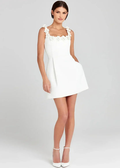 Black - Black structured crepe mini dress featuring a tailored bodice, A-line skirt with side pockets, and contrasting white 3D floral appliqués along the square neckline and shoulder straps.