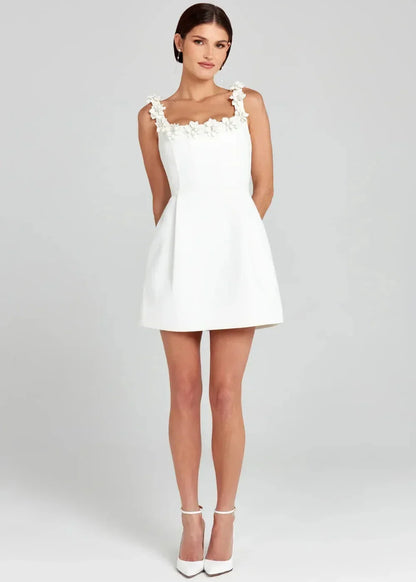 Black - Black structured crepe mini dress featuring a tailored bodice, A-line skirt with side pockets, and contrasting white 3D floral appliqués along the square neckline and shoulder straps.