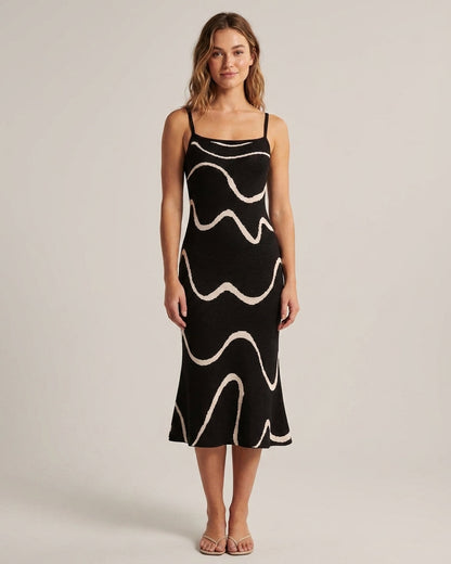 Black - A woman wearing a black knit midi dress featuring a cream abstract wave pattern, thin spaghetti straps, and a square neckline.