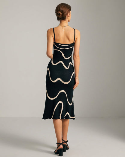 Black - A woman wearing a black knit midi dress featuring a cream abstract wave pattern, thin spaghetti straps, and a square neckline.