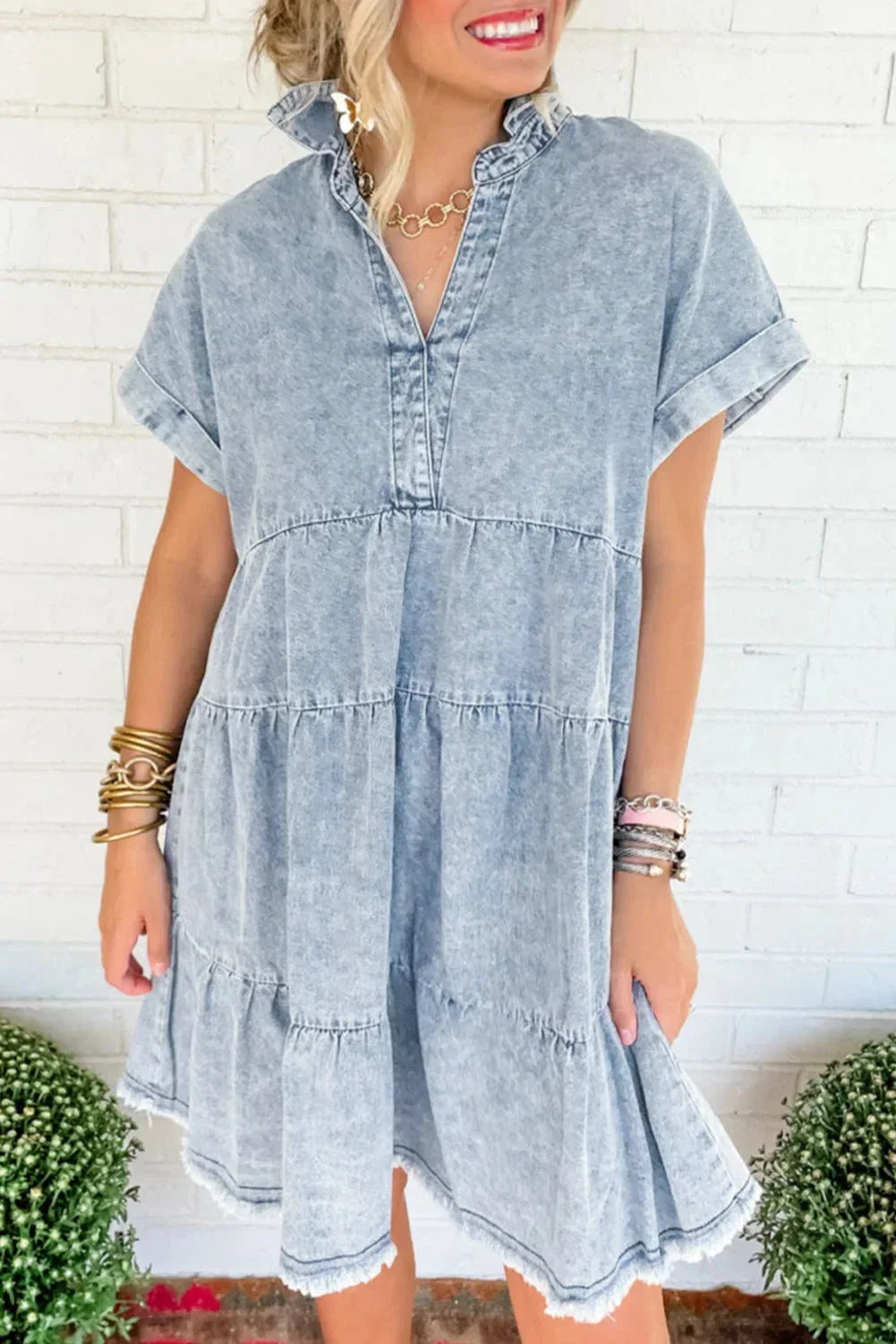 Woman wearing a light blue acid wash denim tiered mini dress with short sleeves and a frayed hem.