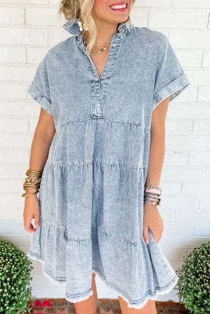 Woman wearing a light blue acid wash denim tiered mini dress with short sleeves and a frayed hem.