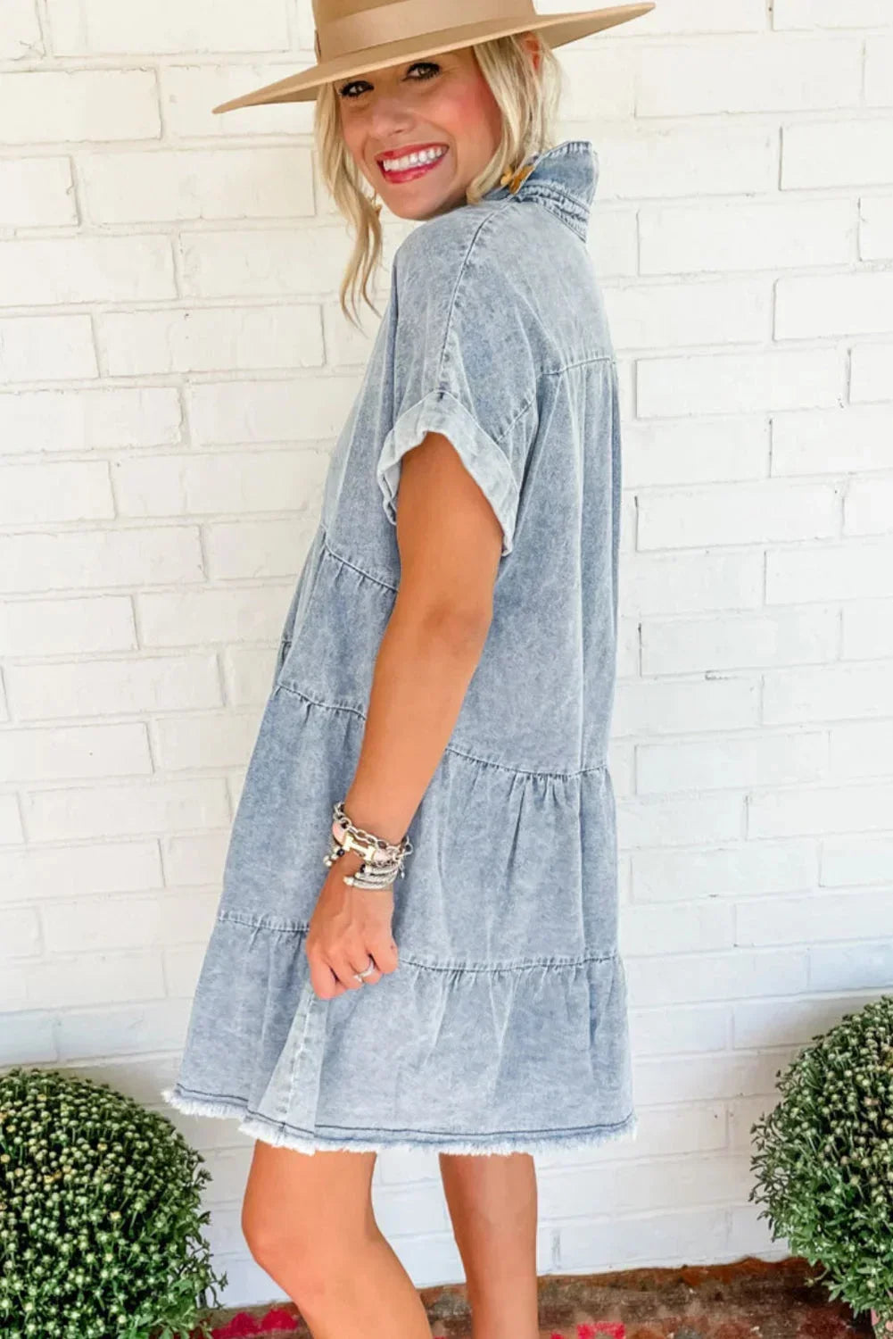 Woman wearing a light blue acid wash denim tiered mini dress with short sleeves and a frayed hem.