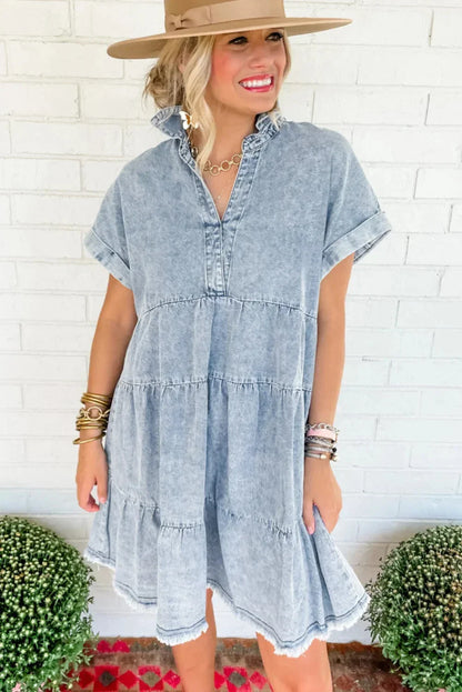 Woman wearing a light blue acid wash denim tiered mini dress with short sleeves and a frayed hem.