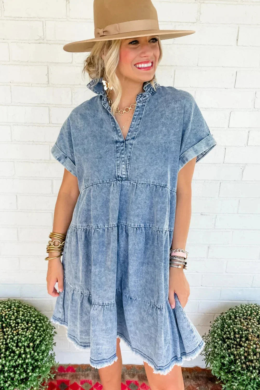 Woman wearing a light blue acid wash denim tiered mini dress with short sleeves and a frayed hem.