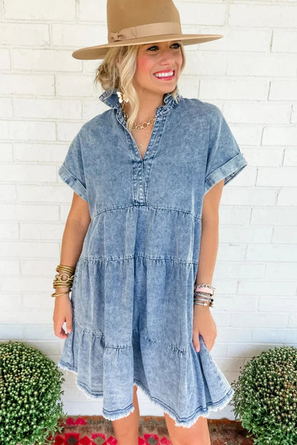 Woman wearing a light blue acid wash denim tiered mini dress with short sleeves and a frayed hem.