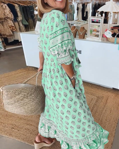 Pink - A woman wearing a light blue block-print maxi dress with a split V-neckline, tassel ties, and tiered skirt, holding a woven straw tote bag.
