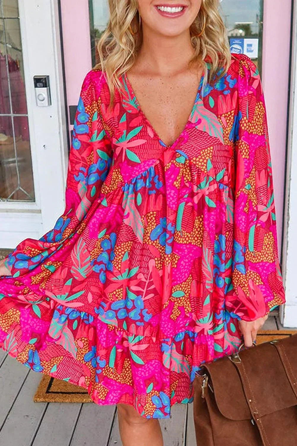 rose - Woman wearing a bright pink abstract botanical print mini dress with a v-neckline, long balloon sleeves, and a tiered babydoll skirt.