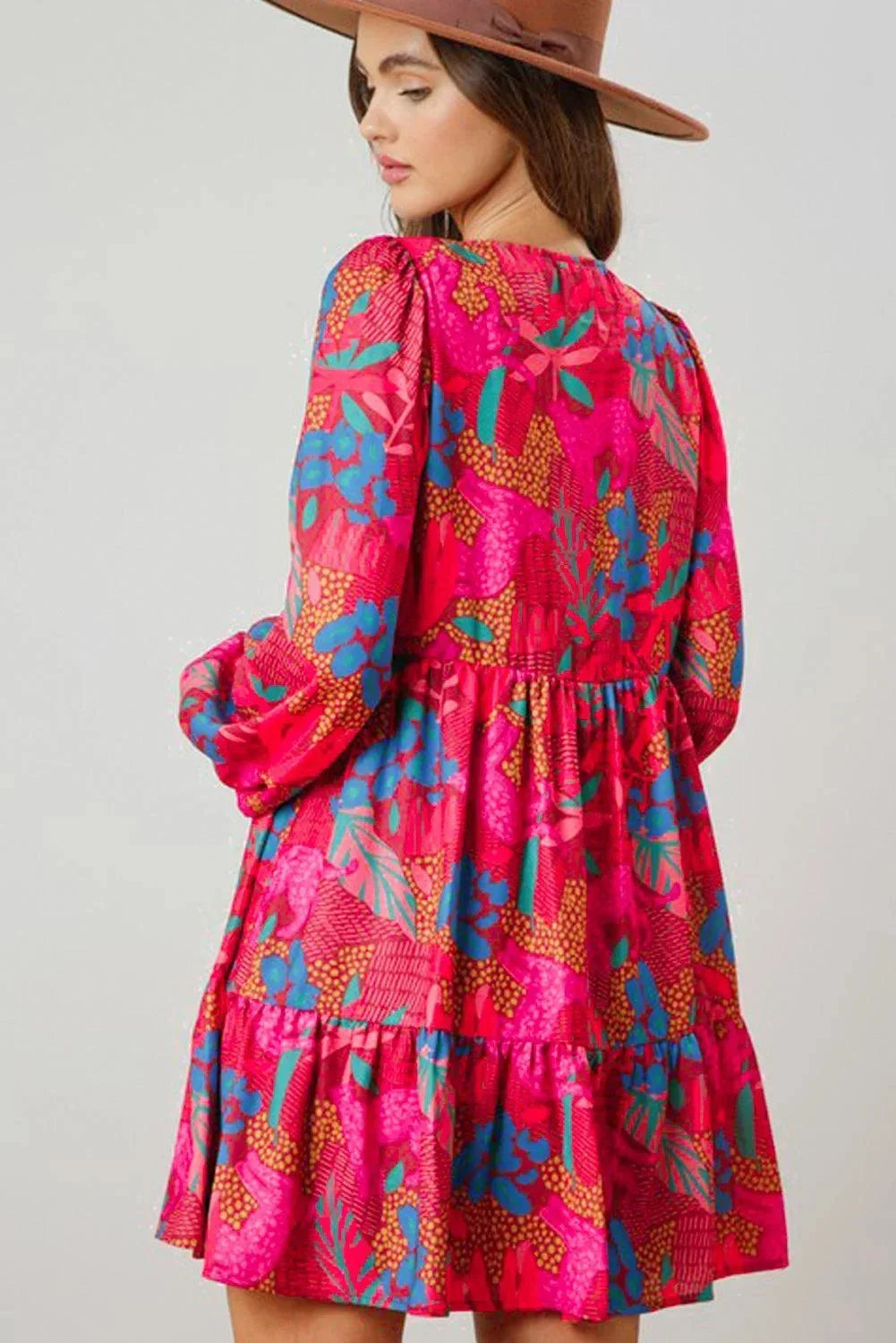 rose - Woman wearing a bright pink abstract botanical print mini dress with a v-neckline, long balloon sleeves, and a tiered babydoll skirt.