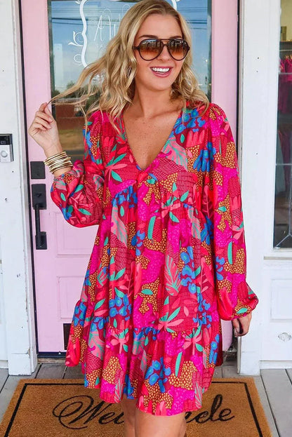 rose - Woman wearing a bright pink abstract botanical print mini dress with a v-neckline, long balloon sleeves, and a tiered babydoll skirt.