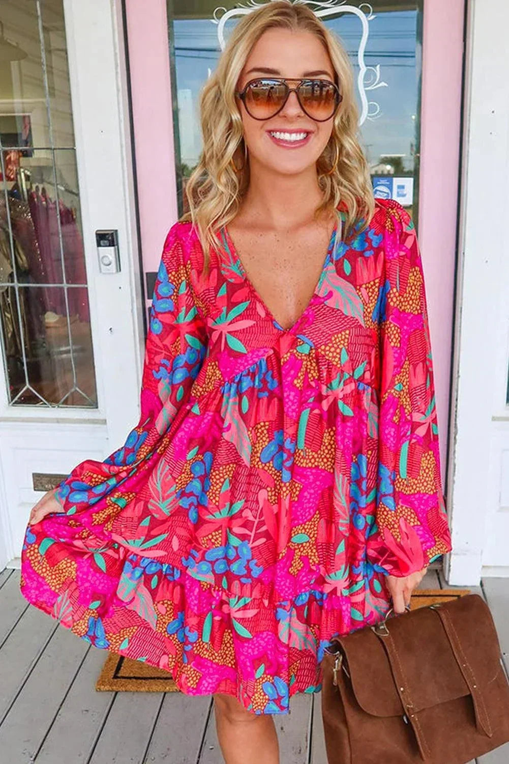 rose - Woman wearing a bright pink abstract botanical print mini dress with a v-neckline, long balloon sleeves, and a tiered babydoll skirt.