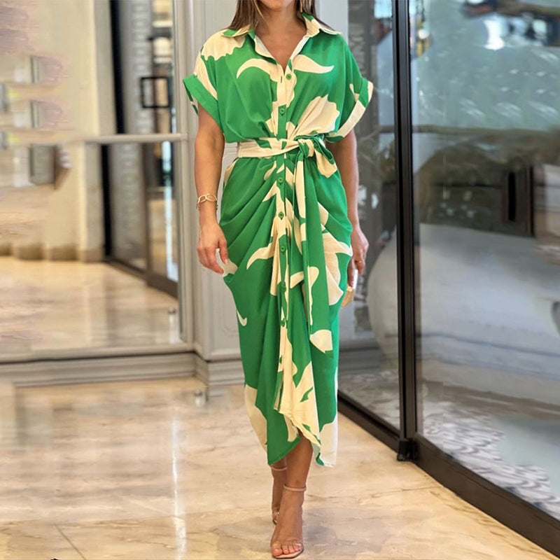 Green - A woman wearing a green and cream botanical print midi shirt dress with a button-down front, belted waist, and draped skirt detail.