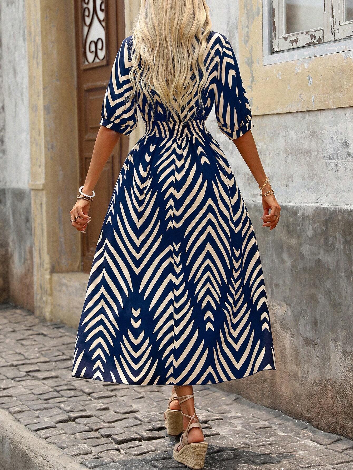 Blue - A woman wearing a navy and cream chevron print maxi dress with a smocked waist, V-neckline, puff sleeves, and a high side slit, paired with lace-up sandals.