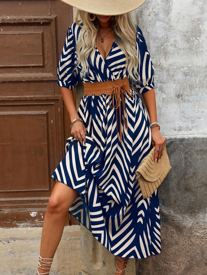 Blue - A woman wearing a navy and cream chevron print maxi dress with a smocked waist, V-neckline, puff sleeves, and a high side slit, paired with lace-up sandals.