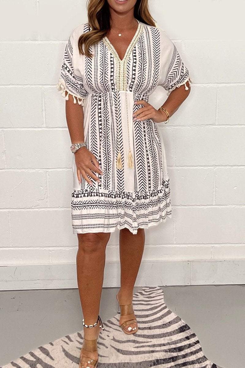 Black White - A woman wearing a white mini dress with blue chevron and geometric prints, featuring a V-neckline with tassel ties, flutter sleeves with tassel trim, and an empire waist.