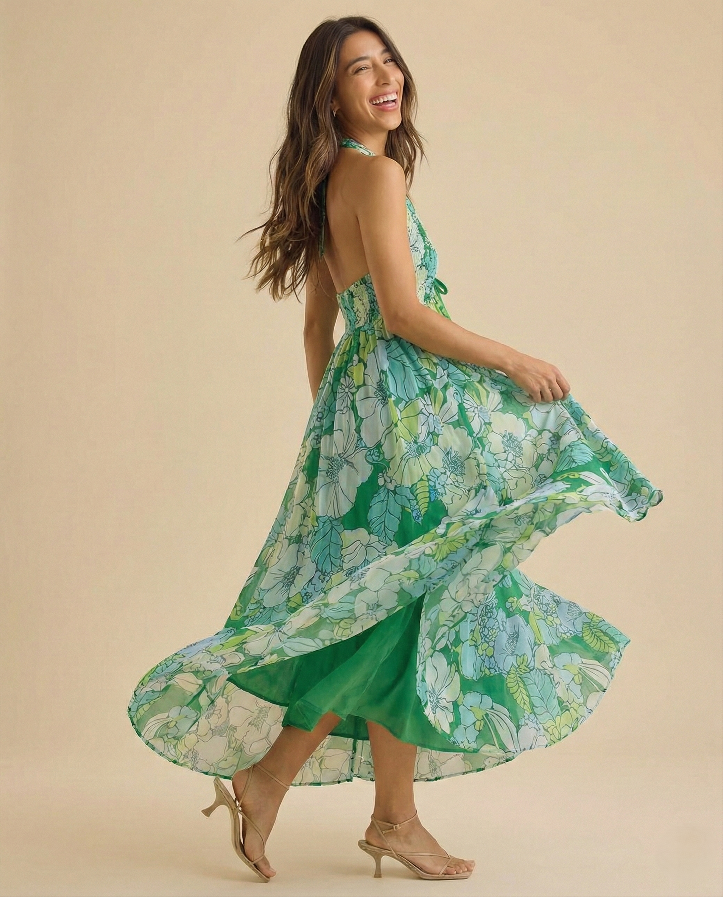 Ivy - A woman wearing a pastel floral print chiffon maxi dress with a smocked halter bodice, tie-neck detail, and a flowing skirt with a side slit.