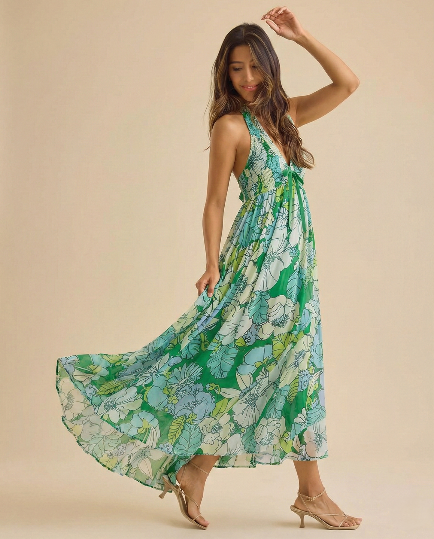 Ivy - A woman wearing a pastel floral print chiffon maxi dress with a smocked halter bodice, tie-neck detail, and a flowing skirt with a side slit.