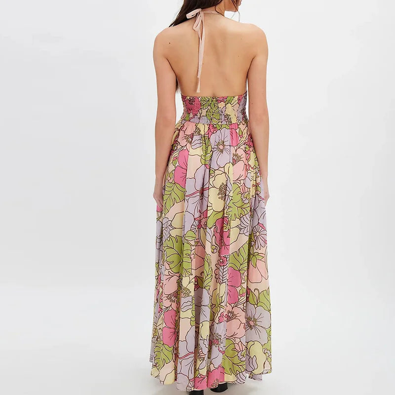 Ivy - A woman wearing a pastel floral print chiffon maxi dress with a smocked halter bodice, tie-neck detail, and a flowing skirt with a side slit.