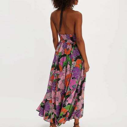 Ivy - A woman wearing a pastel floral print chiffon maxi dress with a smocked halter bodice, tie-neck detail, and a flowing skirt with a side slit.