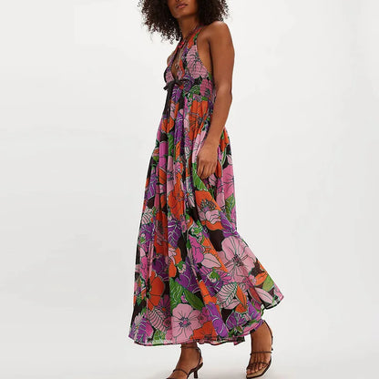 Ivy - A woman wearing a pastel floral print chiffon maxi dress with a smocked halter bodice, tie-neck detail, and a flowing skirt with a side slit.