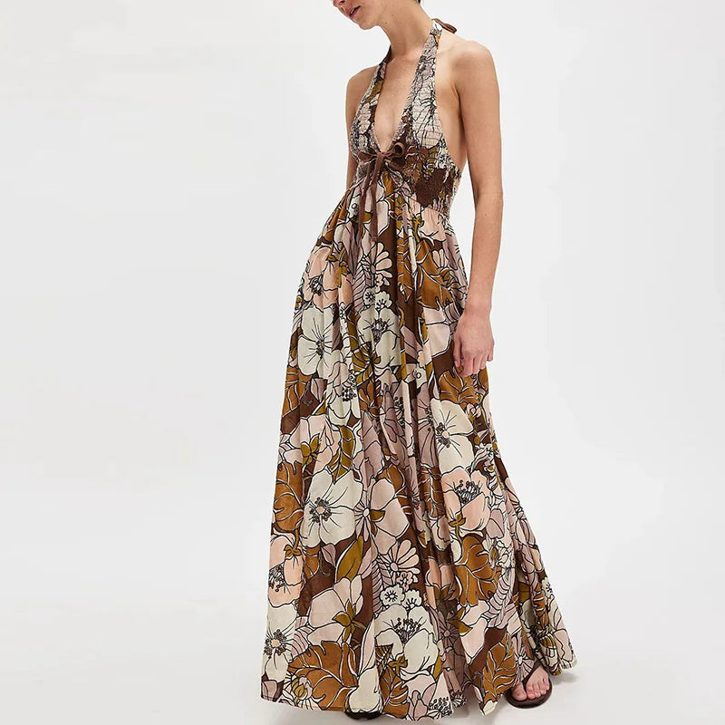 Ivy - A woman wearing a pastel floral print chiffon maxi dress with a smocked halter bodice, tie-neck detail, and a flowing skirt with a side slit.