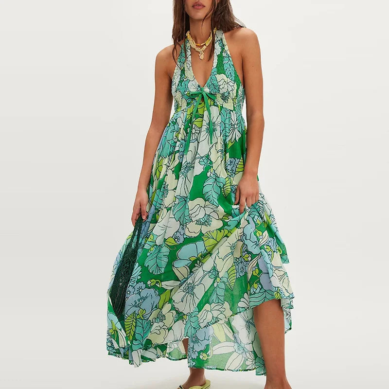 Ivy - A woman wearing a pastel floral print chiffon maxi dress with a smocked halter bodice, tie-neck detail, and a flowing skirt with a side slit.