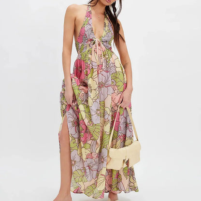 Ivy - A woman wearing a pastel floral print chiffon maxi dress with a smocked halter bodice, tie-neck detail, and a flowing skirt with a side slit.