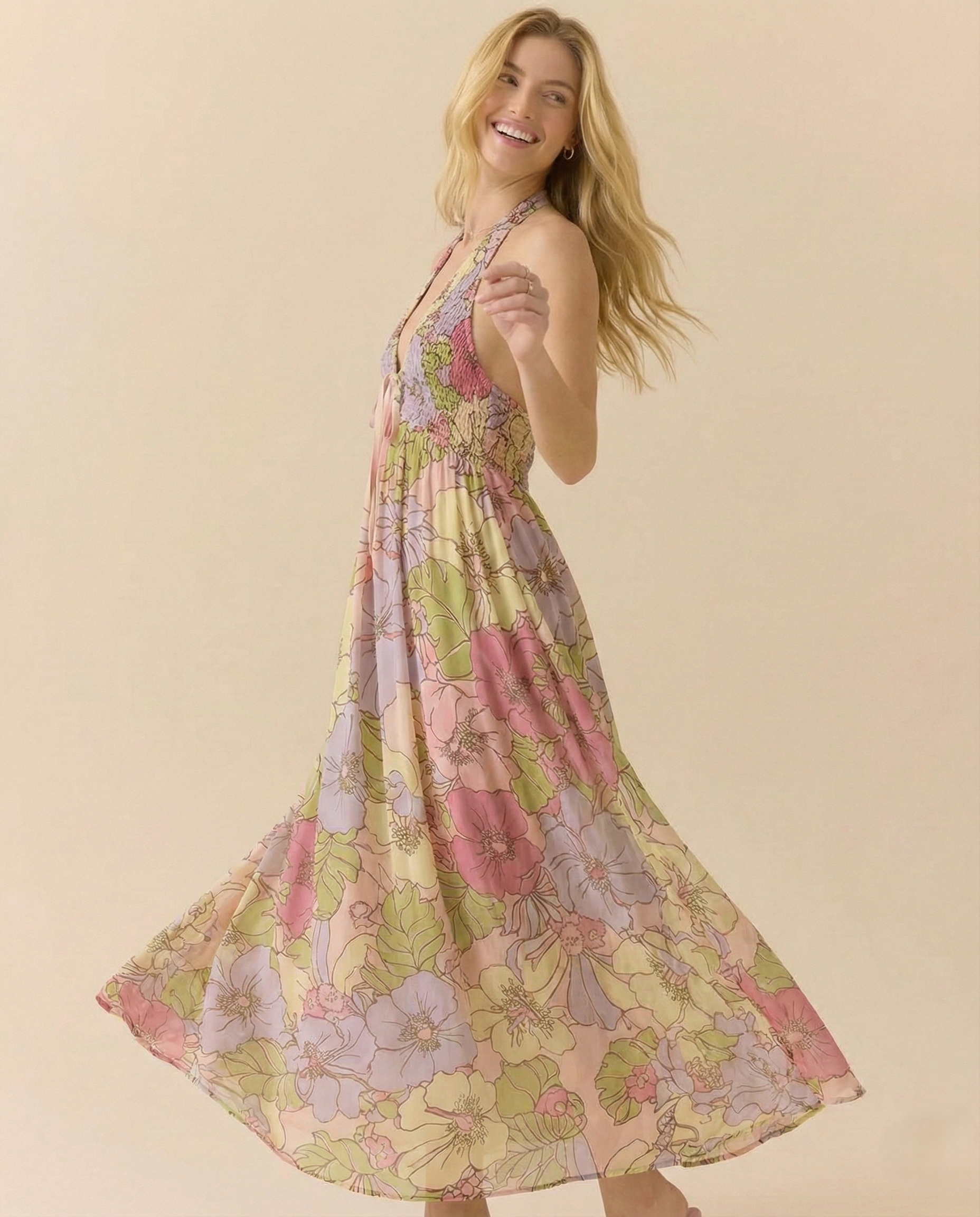 Garden - A woman wearing a pastel floral print chiffon maxi dress with a smocked halter bodice, tie-neck detail, and a flowing skirt with a side slit.
