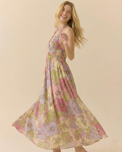 Garden - A woman wearing a pastel floral print chiffon maxi dress with a smocked halter bodice, tie-neck detail, and a flowing skirt with a side slit.