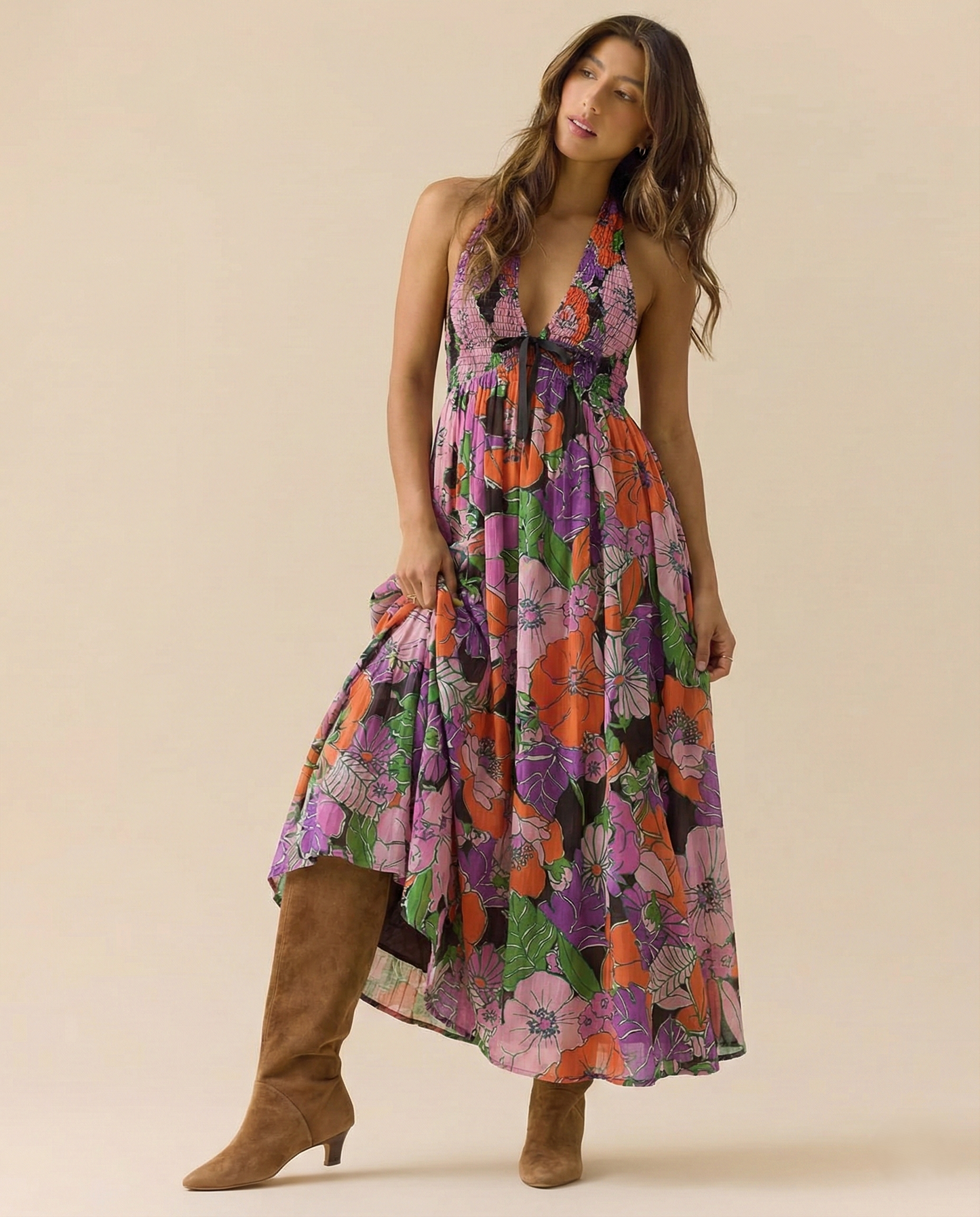 Tropical - A woman wearing a pastel floral print chiffon maxi dress with a smocked halter bodice, tie-neck detail, and a flowing skirt with a side slit.