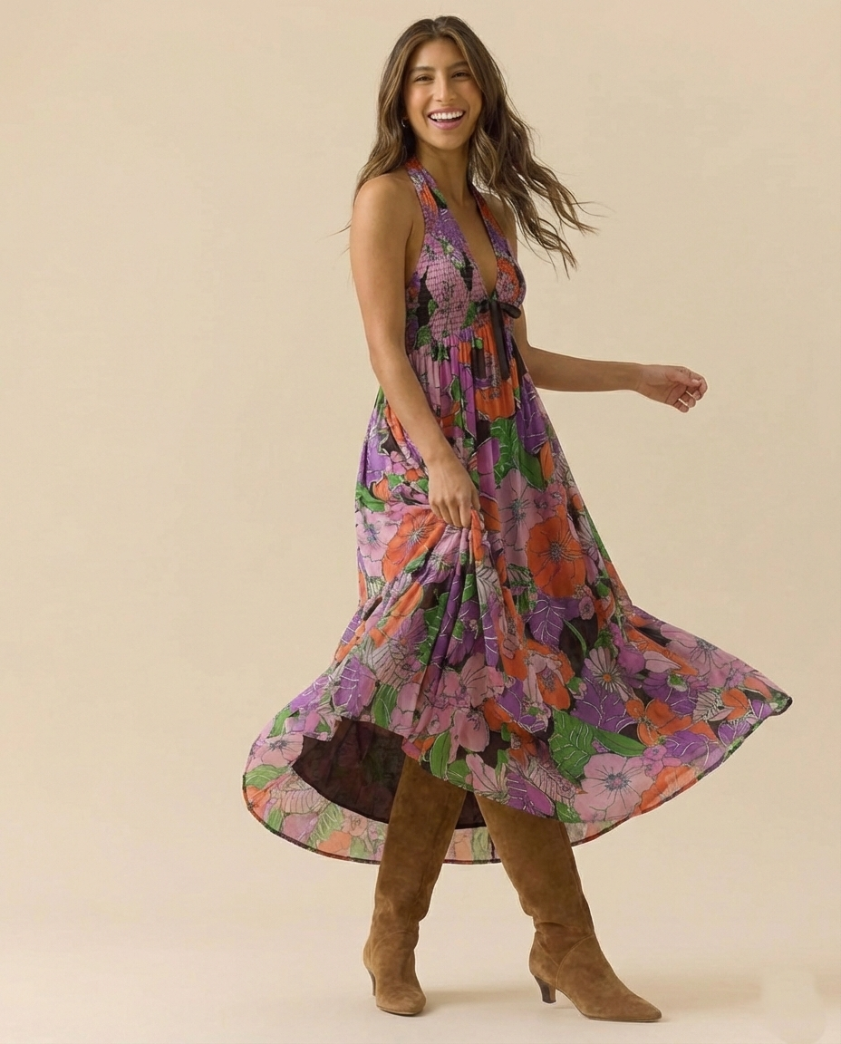 Tropical - A woman wearing a pastel floral print chiffon maxi dress with a smocked halter bodice, tie-neck detail, and a flowing skirt with a side slit.