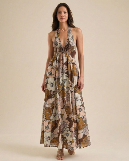 Autumn - A woman wearing a pastel floral print chiffon maxi dress with a smocked halter bodice, tie-neck detail, and a flowing skirt with a side slit.