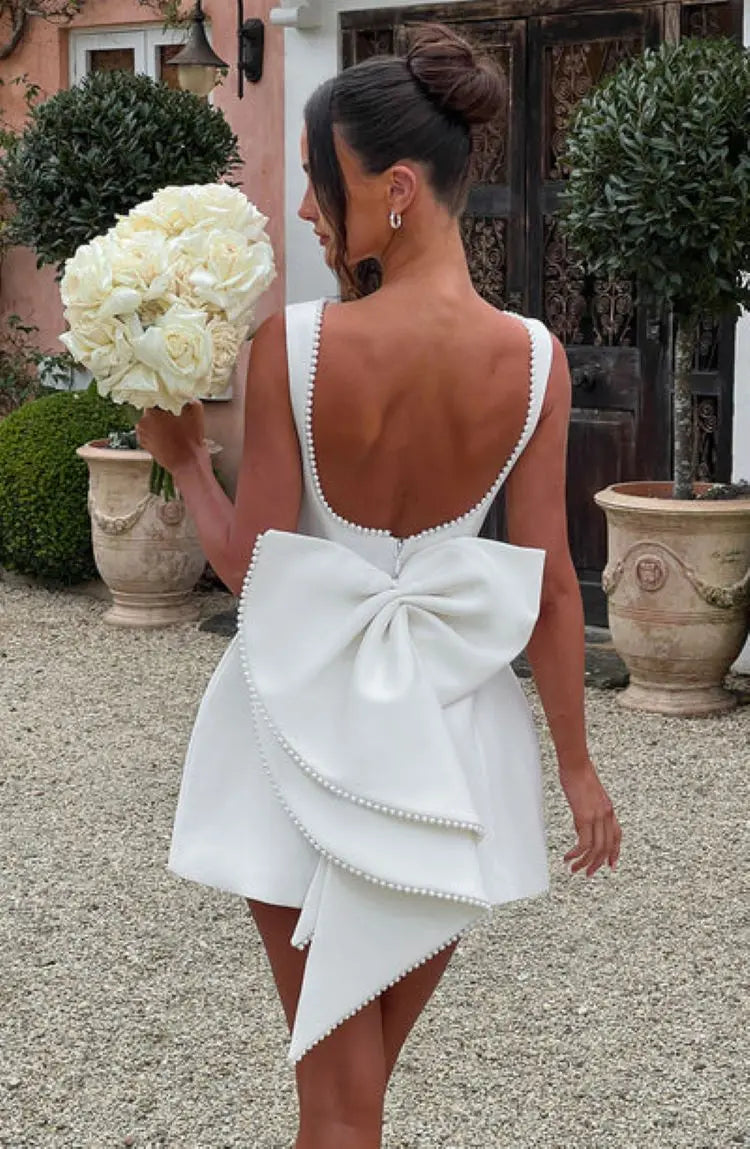 Black - Sleeveless crepe mini dress featuring a pearl-embellished bateau neckline, tailored princess seams, and a large structured back bow.