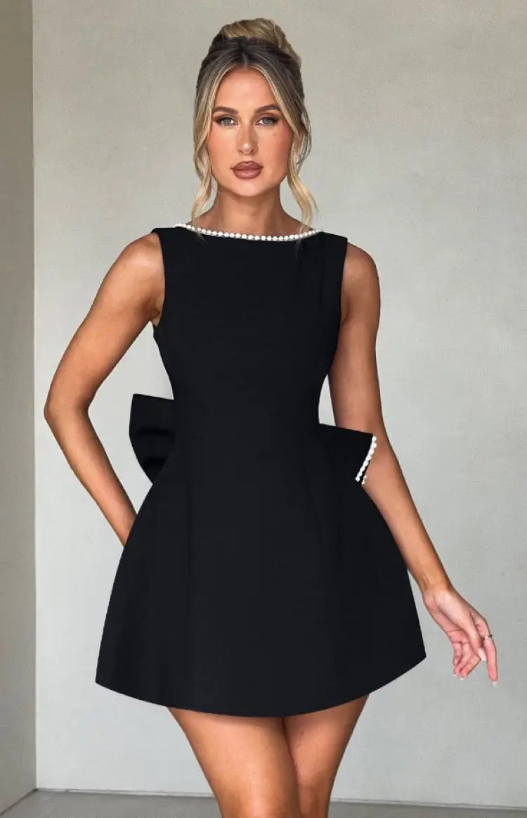 Black - Sleeveless crepe mini dress featuring a pearl-embellished bateau neckline, tailored princess seams, and a large structured back bow.