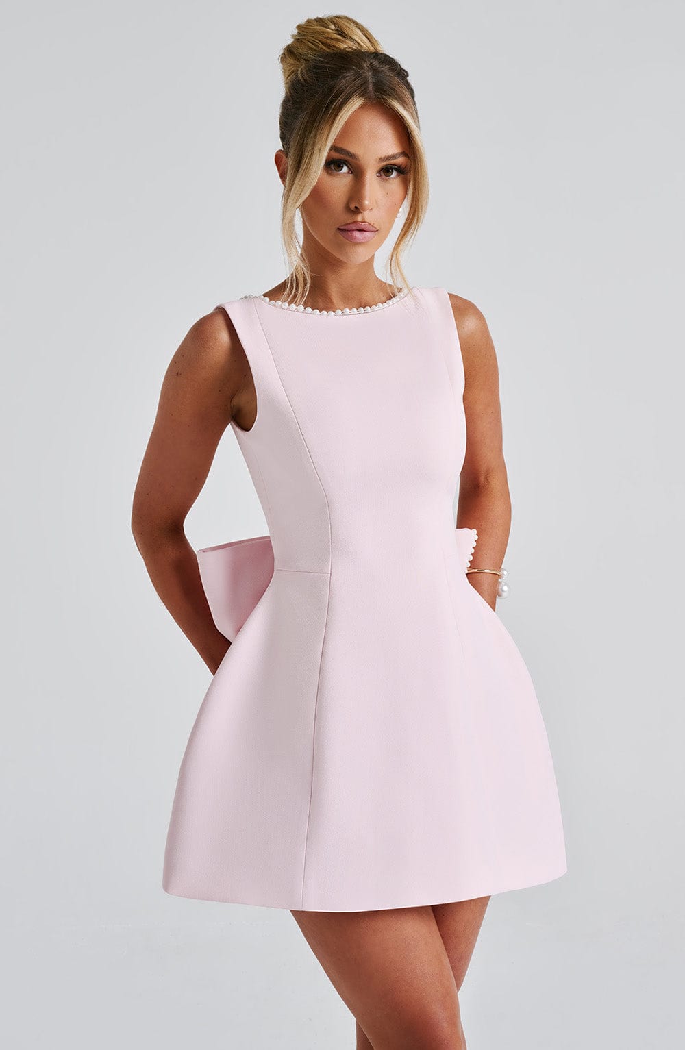Black - Sleeveless crepe mini dress featuring a pearl-embellished bateau neckline, tailored princess seams, and a large structured back bow.