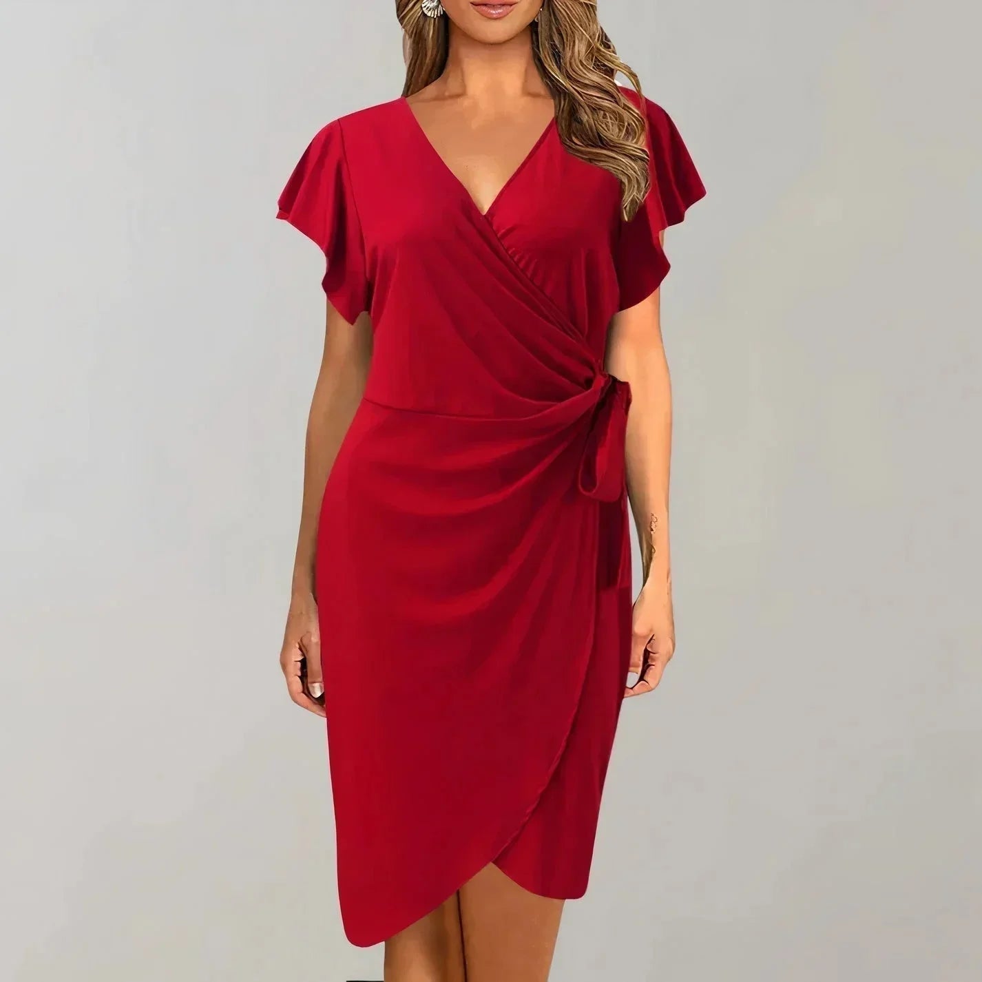 Red - Solid red crepe midi dress featuring a surplice V-neckline, short flutter sleeves, a ruched side tie waist, and an asymmetrical tulip hem.