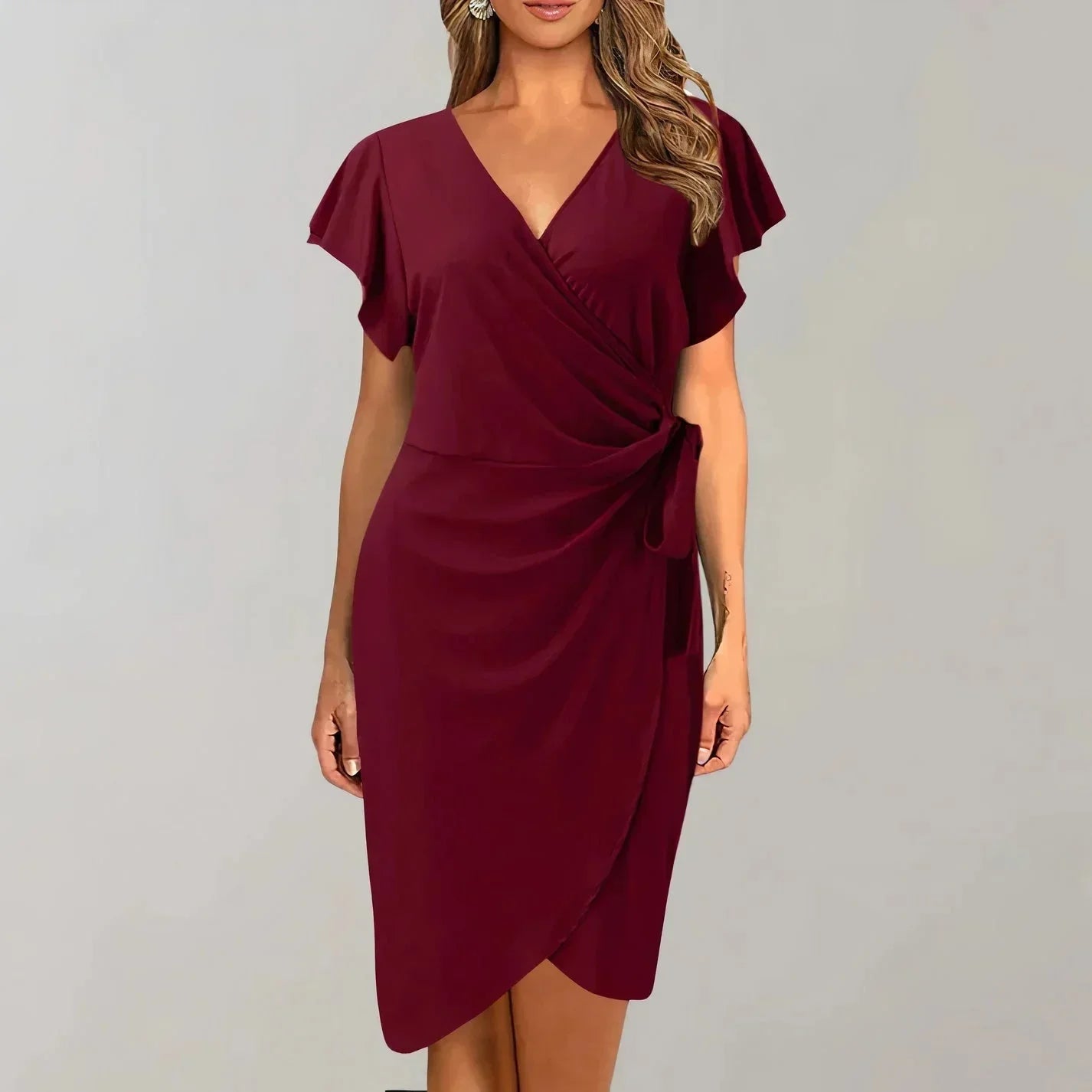 Deep red - Solid red crepe midi dress featuring a surplice V-neckline, short flutter sleeves, a ruched side tie waist, and an asymmetrical tulip hem.